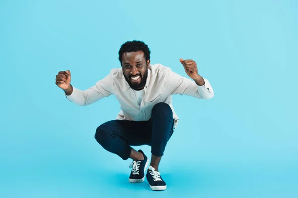 Excité homme afro-américain barbu assis isolé sur bleu — Photo de stock