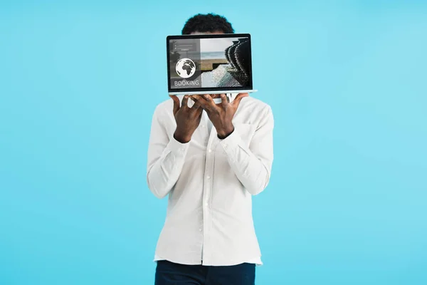 Афроамериканський чоловік показує ноутбук з веб-сайтом бронювання ізольовано на синьому — стокове фото