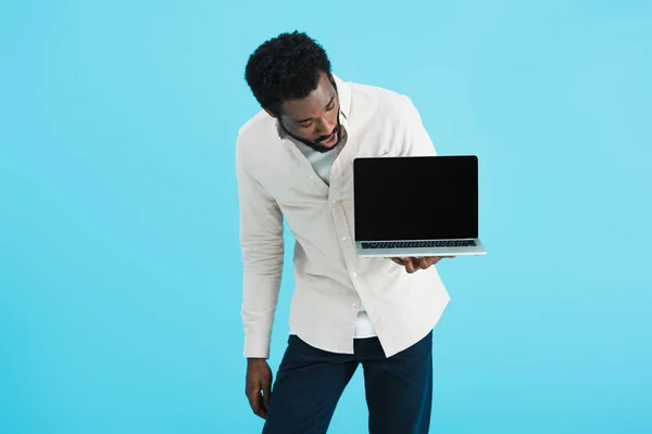 Sorpreso uomo afroamericano mostrando laptop con schermo bianco isolato su blu — Foto stock