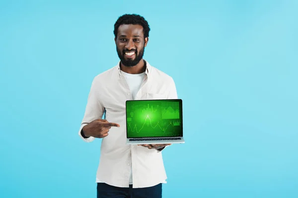 Homme afro-américain souriant pointant vers un ordinateur portable avec un graphique isolé sur bleu — Photo de stock