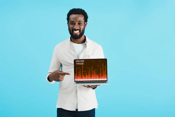 Souriant homme afro-américain pointant vers un ordinateur portable avec commerce en ligne isolé sur bleu — Photo de stock