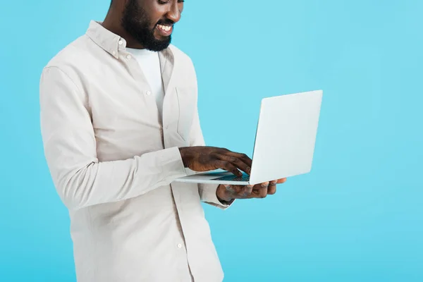 Sonriente afroamericano hombre usando portátil aislado en azul - foto de stock