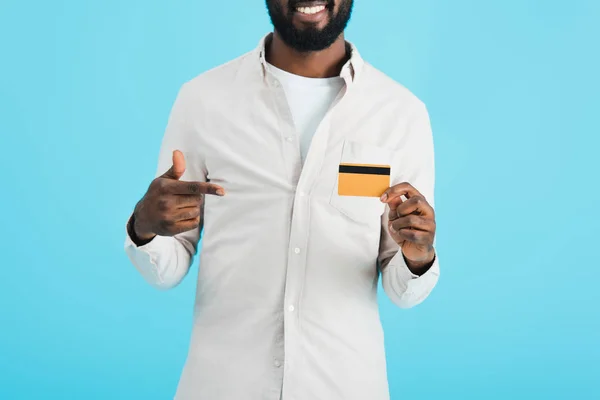 Recortado vista de sonriente afroamericano hombre apuntando a la tarjeta de crédito aislado en azul - foto de stock