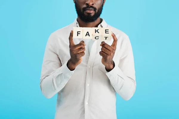 Vista cortada do homem americano africano que prende blocos do alfabeto com a palavra do fato, isolada no azul — Fotografia de Stock