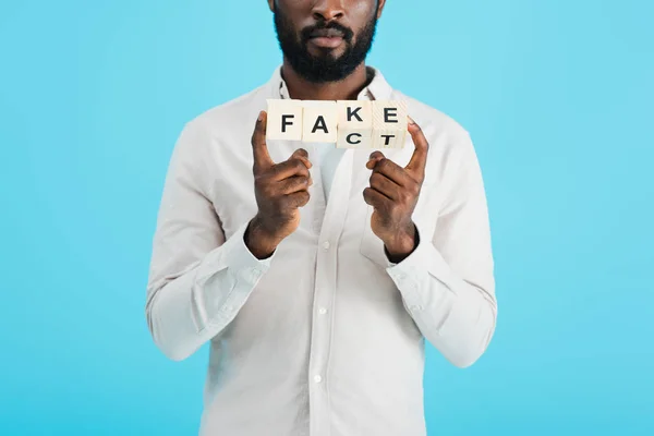 Cropped view of african american man holding alphabet blocks with fact word, isolated on blue — Stock Photo