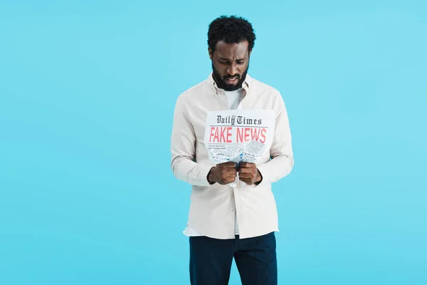 Souligné homme afro-américain lecture journal avec de fausses nouvelles isolé sur bleu — Photo de stock