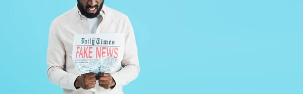 Cropped view of stressed african american man reading newspaper with fake news isolated on blue — Stock Photo