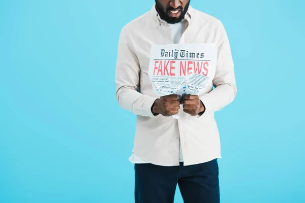 Abgeschnittene Ansicht eines wütenden afrikanisch-amerikanischen Mannes, der Zeitung liest, mit Fake News isoliert auf blau — Stockfoto