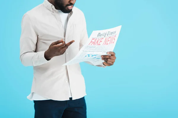 Vista cortada de homem americano africano agressivo lendo jornal com notícias falsas e mostrando dedo médio isolado no azul — Fotografia de Stock