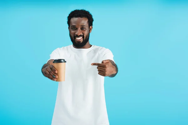 Souriant homme afro-américain tenant pointant du doigt le café à emporter, isolé sur bleu — Photo de stock