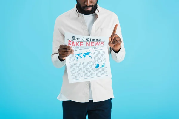 Vue recadrée d'un homme afro-américain en colère lisant un journal avec de fausses nouvelles et pointant vers le haut isolé sur bleu — Photo de stock