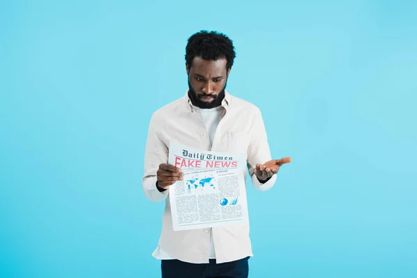 Confused african american man reading newspaper with fake news isolated on blue — Stock Photo