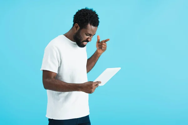 Сердитий афроамериканський чоловік використовує цифровий планшет ізольований на синьому — стокове фото