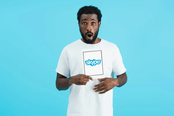 KYIV, UCRANIA - 17 DE MAYO DE 2019: sorprendido hombre afroamericano mostrando tableta digital con aplicación skype, aislado en azul - foto de stock