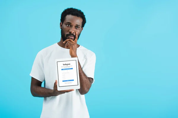 Kyiv, ukraine - 17. Mai 2019: nachdenklicher afrikanisch-amerikanischer Mann zeigt digitales Tablet mit Instagram-App, isoliert auf blau — Stockfoto