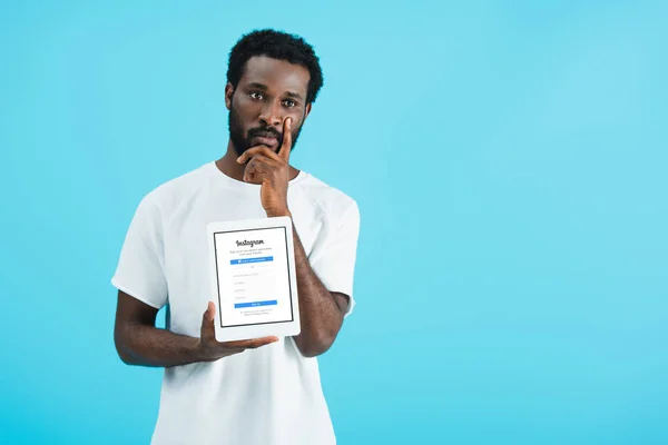 KYIV, UKRAINE - MAY 17, 2019: thoughtful african american man showing digital tablet with instagram app, isolated on blue — Stock Photo