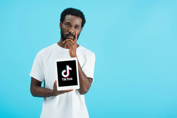 KYIV, UCRAINA - 17 MAGGIO 2019: uomo afroamericano riflessivo che mostra tablet digitale con app Tik Tok, isolato sul blu — Foto stock