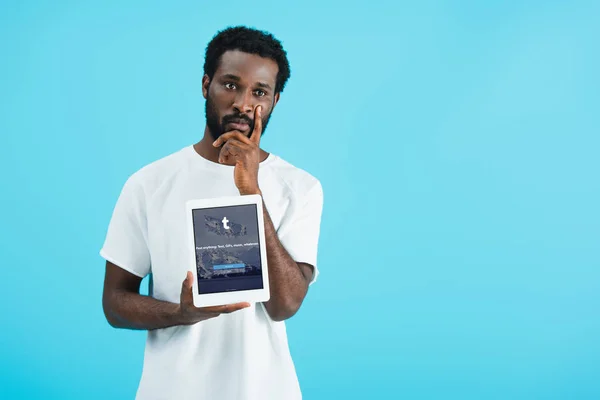 KYIV, UCRANIA - 17 DE MAYO DE 2019: hombre afroamericano reflexivo mostrando tableta digital con aplicación tumblr, aislado en azul - foto de stock