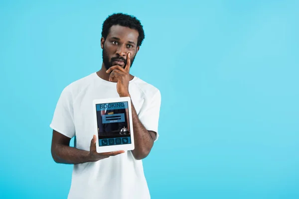 Hombre afroamericano reflexivo mostrando tableta digital con aplicación de reserva, aislado en azul - foto de stock