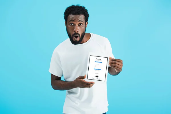 KYIV, UCRANIA - 17 DE MAYO DE 2019: sorprendido hombre afroamericano mostrando tableta digital con aplicación instagram, aislado en azul - foto de stock
