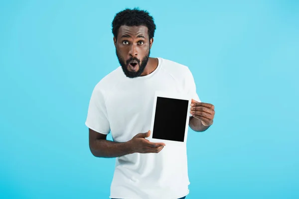 Sorprendido hombre afroamericano mostrando tableta digital con pantalla en blanco aislado en azul - foto de stock