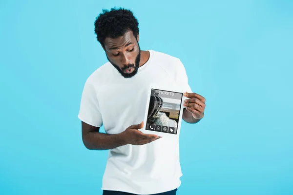 Sorprendido hombre afroamericano mostrando tableta digital con la aplicación de boletos, aislado en azul - foto de stock