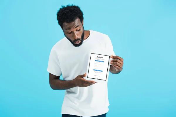KYIV, UKRAINE - MAIO 17, 2019: homem afro-americano chocado olhando para tablet digital com aplicativo instagram, isolado em azul — Fotografia de Stock