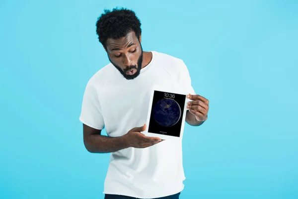 KYIV, UCRANIA - 17 de mayo de 2019: sorprendido hombre afroamericano mirando la tableta digital, aislado en azul - foto de stock