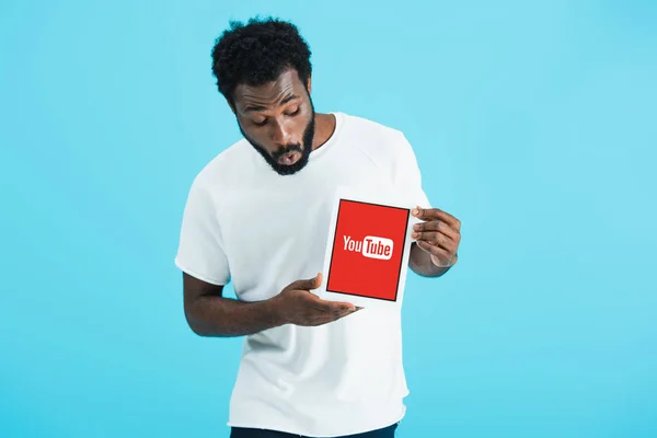 KYIV, UCRAINA - 17 MAGGIO 2019: uomo afroamericano scioccato che guarda tablet digitale con app youtube, isolato su blu — Foto stock