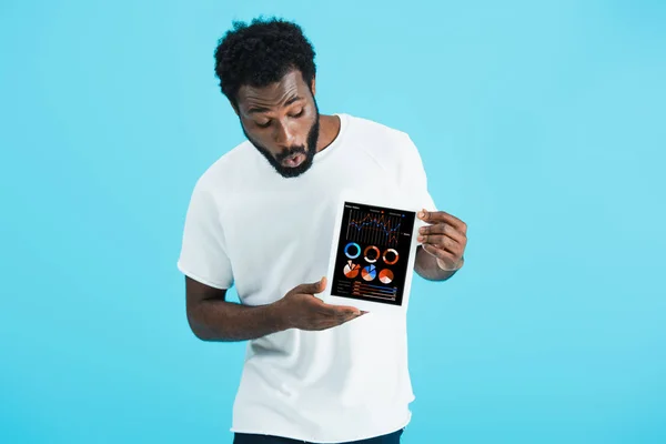 Шокированный африканский американец показывает цифровой планшет с инфографическим приложением, изолированным на голубом — стоковое фото