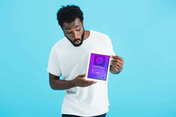 Choqué homme afro-américain montrant tablette numérique avec application shopping, isolé sur bleu — Photo de stock