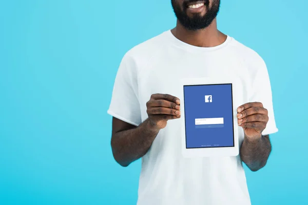 KYIV, UKRAINE - MAY 17, 2019: cropped view of african american man showing digital tablet with facebook app, isolated on blue — Stock Photo