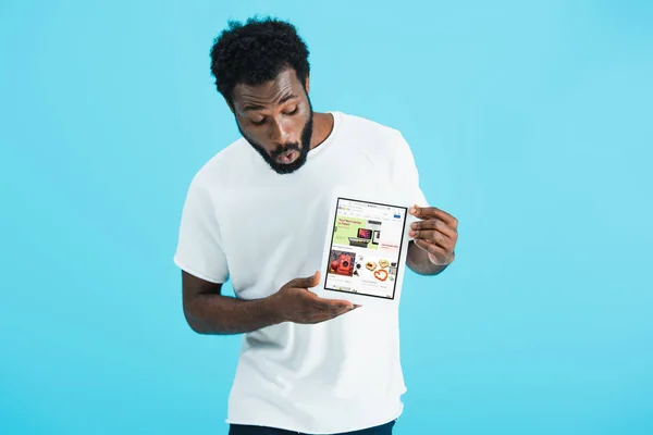 Kyiv, ukraine - 17. Mai 2019: schockierter afrikanisch-amerikanischer Mann blickt auf digitales Tablet mit ebay-App, isoliert auf blau — Stockfoto