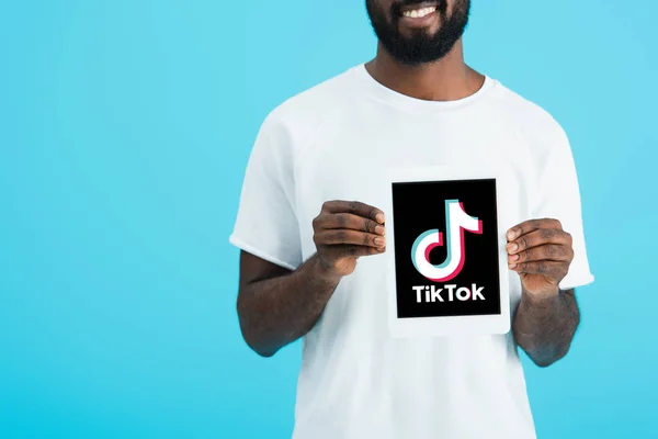 KYIV, UCRAINA - 17 MAGGIO 2019: vista ritagliata dell'uomo afroamericano che mostra tablet digitale con app Tik Tok, isolato su blu — Foto stock