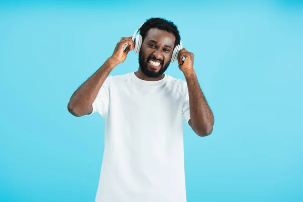 Handsome cheerful african american man listening music with headphones, isolated on blue — Stock Photo