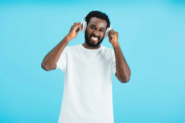 Guapo alegre afroamericano hombre escuchando música con auriculares, aislado en azul - foto de stock