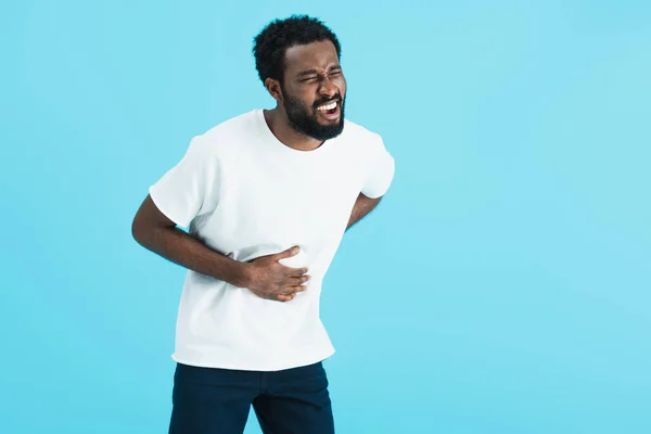 Young african american man in white t-shirt having abdominal pain, isolated on blue — Stock Photo