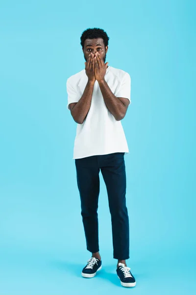 Worried african american man in white t-shirt closing face, isolated on blue — Stock Photo