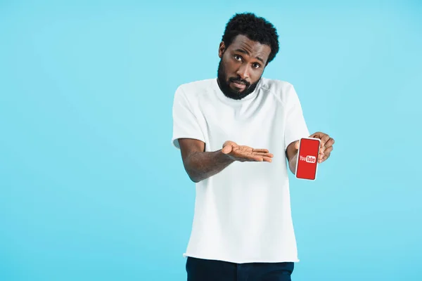 KYIV, UKRAINE - MAY 17, 2019: frustrated african american man showing smartphone with youtube app, isolated on blue — Stock Photo