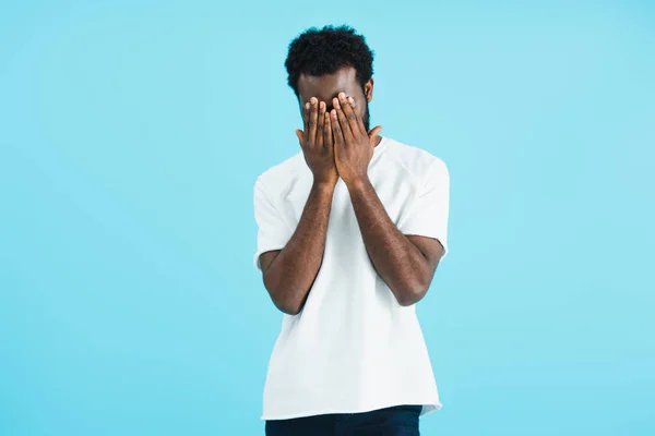 Frustrated african american man in white t-shirt closing face, isolated on blue — Stock Photo