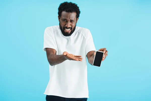 Hombre afroamericano asustado mostrando teléfono inteligente con pantalla en blanco, aislado en azul - foto de stock