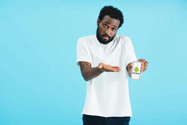 KYIV, UKRAINE - MAY 17, 2019: frustrated african american man showing smartphone with android app, isolated on blue — Stock Photo