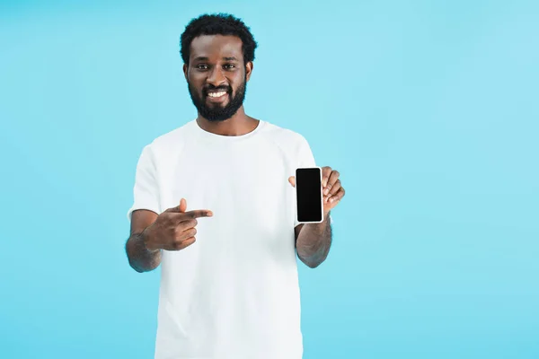 Веселий афроамериканський чоловік вказує на смартфон з порожнім екраном, ізольований на синьому — стокове фото