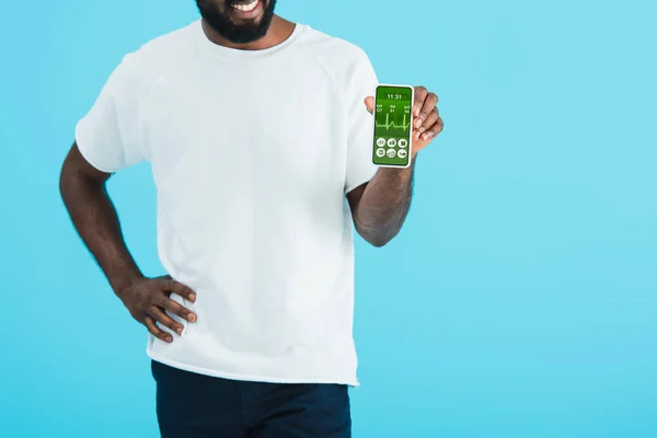 Vista recortada del hombre afroamericano que muestra el teléfono inteligente con aplicación de salud, aislado en azul - foto de stock