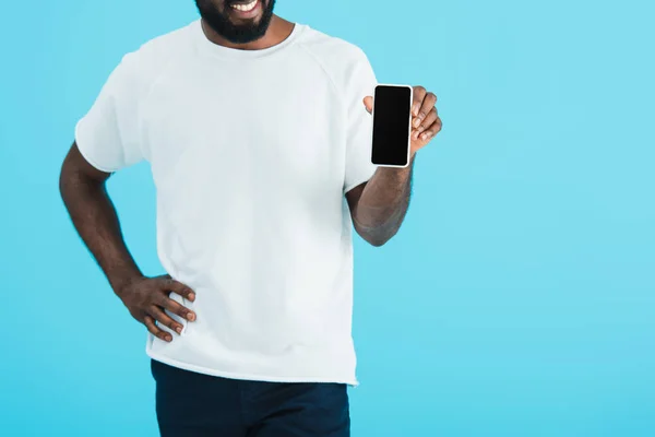 Vista recortada del hombre afroamericano que muestra el teléfono inteligente con pantalla en blanco, aislado en azul - foto de stock