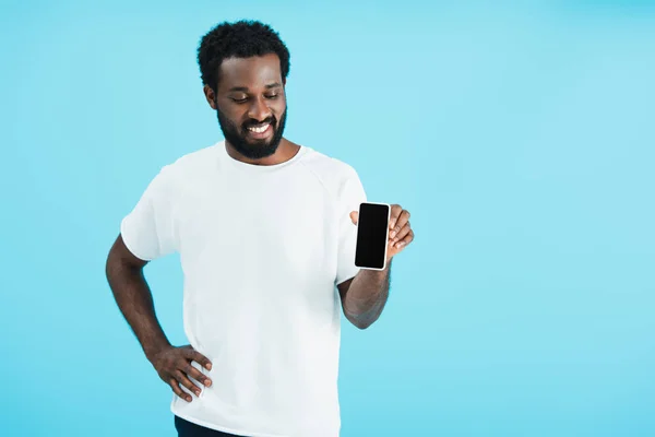 Hombre afroamericano feliz mostrando teléfono inteligente con pantalla en blanco, aislado en azul - foto de stock