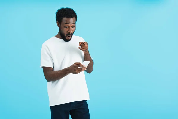 Sorprendido hombre afroamericano usando teléfono inteligente, aislado en azul - foto de stock