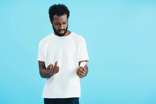Сердитый африканский американец, показывающий средний палец смартфону, изолированный на голубом — стоковое фото