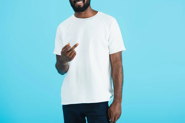 Recortado vista de sonriente afroamericano hombre mostrando el dedo medio aislado en azul - foto de stock