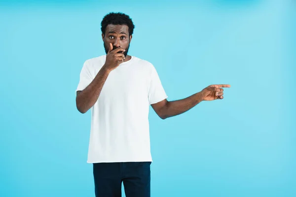 Shocked african american man in white t-shirt pointing aside isolated on blue — Stock Photo